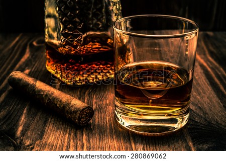 Decanter of whiskey and a glass with cuban cigar on a wooden table. Angle view, image vignetting and the orange-blue toning