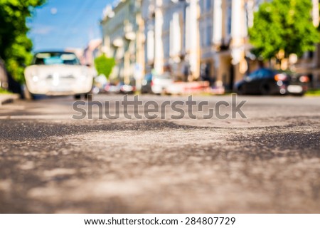 City on a sunny day, a quiet street after rain with trees and cars. View from the level of asphalt
