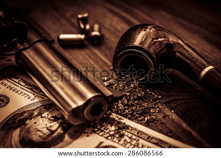 Money and a gun with a pipe on a wooden table. Image vignetting and the yellow-orange toning