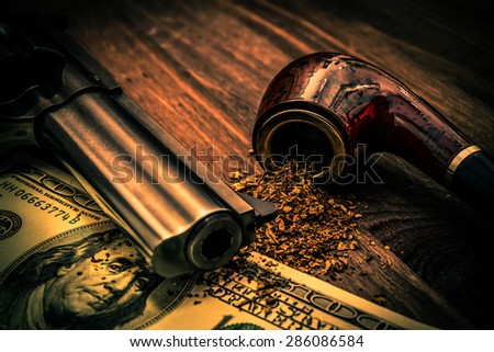Money and a gun with a pipe on a wooden table. Image vignetting and the orange-blue toning