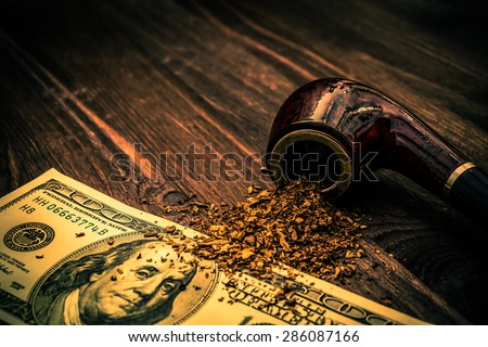 Tube for smoking tobacco and money on a wooden table. Image vignetting and the orange-blue toning