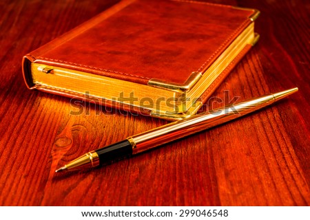 Golden pen with a leather diary on a mahogany table