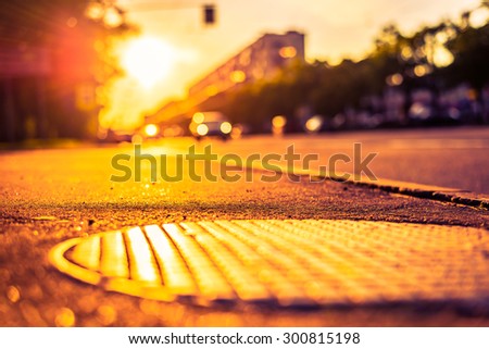 Sunny day in the city, view from the sidewalk level of the hatch at the lights of a car driving up. Image in the orange-purple toning