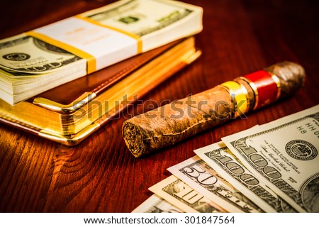 Money with a leather diary and cuban cigar on a mahogany table. Image vignetting and hard tones