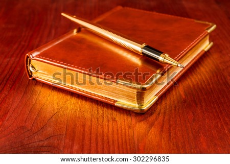 Golden pen on a leather diary on a mahogany table