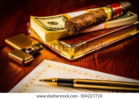 Pack of dollars and cuban cigar on the leather diary with bank check and golden pen on the table. Focus on the cuban cigar, image vignetting and hard tones