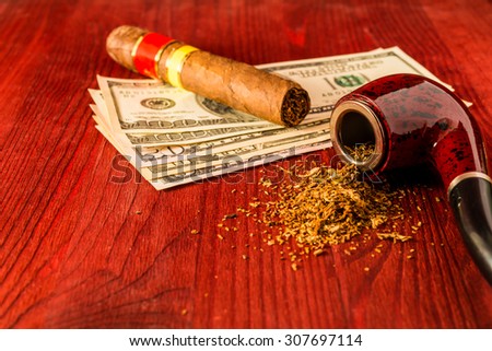 Tube for smoking tobacco and money with cuban cigar on a wooden table. Focus on the tube