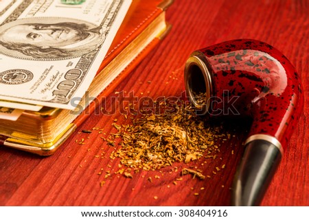 Tube for smoking tobacco and money on the leather diary on a wooden table. Close up view, focus on the tube