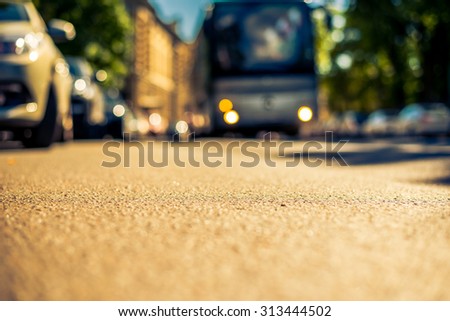 Clear day in the big city, a bus rides through the streets near the park. View from the level of asphalt, image in the yellow-blue toning
