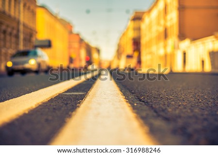 Clear day in the big city, car traveling on an empty city street. View of the road at the level of the dividing line, image in the yellow-blue toning