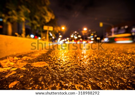 Rainy autumn night in the city, the glowing lights of approaching cars. View from the side of the road at the level of the asphalt