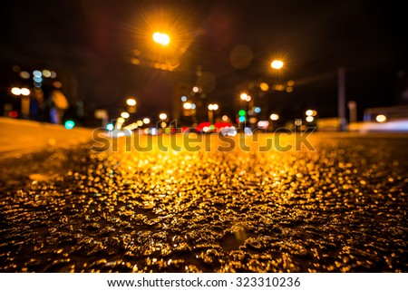 Night city after rain, the glowing lights of approaching cars. View from the side of the road at the level of the asphalt