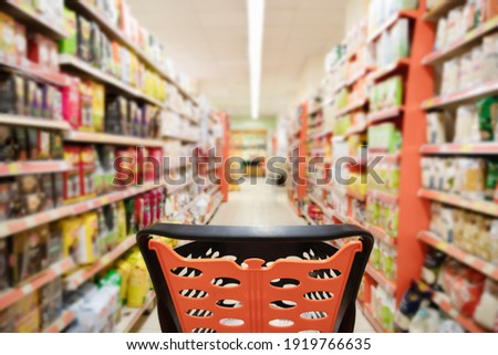 Abstract blurred photo of supermarket with empty shopping cart near packages on shelves in store. Trolley in supermarket and blur product on background.