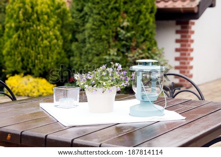 Moody ornamental arrangement with lamp, plant with blue flowers and candle  with natural, green texture in the background