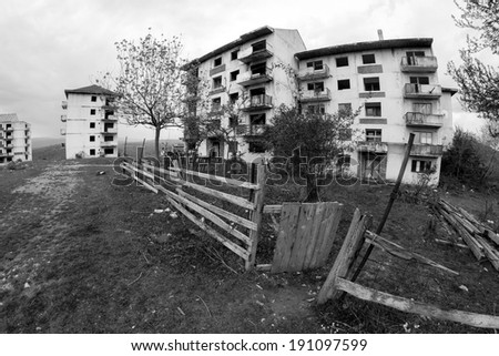 Black and white abandoned block of flats under construction with trees and wooden fence in the backyard