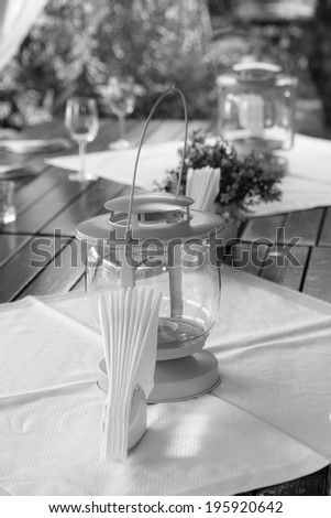 Black and white, moody ornamental arrangement with glasses and napkins with flowers in the background and wooden table