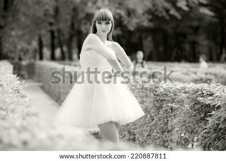 Black and white photo of a beautiful, caucasian, young, long haired woman posing in the park, wearing a white dress, looking happy