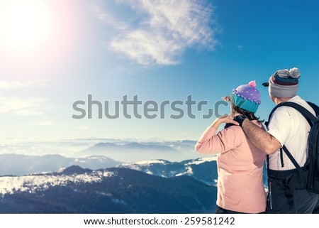 Middle aged couple on the top of the mountain looking away. Direct sunlight, lens flare, warmer tones on highlights. A lot of copy space on the left side of the frame.
