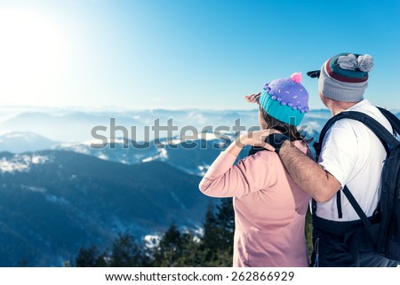 Middle aged couple on the top of the mountain looking away. Direct sunlight, lens flare, warmer tones on highlights. A lot of copy space on the left side of the frame.