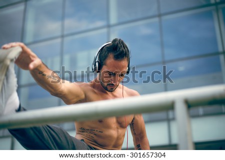 Young man listening to the music and stretching his leg after a heavy workout. Wearing tracksuits without shirt. Selective focus.