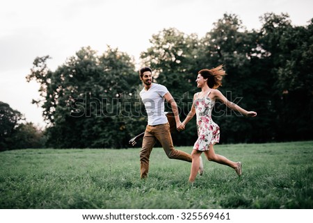 Shot of a young couple holding hands and running through the park. Blurry movement, soft focus