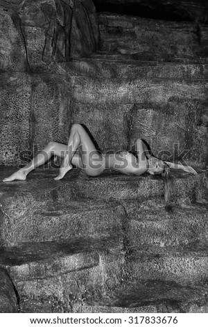 Beautiful blonde model wet sexy muscle woman lying on the mountains, the rocks at the waterfall flies on her water in a wet swimsuit erotic crystals lingerie in Santorini in Greece