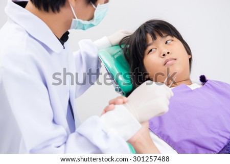 Little girl sitting in the dentists office, Girl frightened by dentists covers her mouth