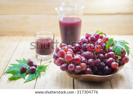 Grape cluster and grape juice with leaves on wood background