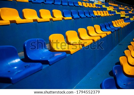 Empty stands, tribune with several raws of plastic blue and yellow seats, chairs for fans at a sport stadium. 商業照片 © 