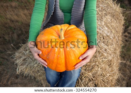 Girl sitting with a pumpkin.Those girls are not seen. Hands girls and pumpkin photographed close up. Underfoot girl autumn mown hay.