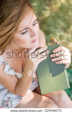 Girl sitting near a tree in the park, holding a book in his hands.  It is in the nature in the park. A girl reading a book, lost in thought, smiling. Close portrait.