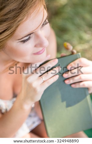 Girl sitting near a tree in the park, holding a book in his hands.  It is in the nature in the park. A girl reading a book, lost in thought, smiling. Close portrait.