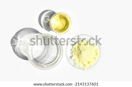 Cosmetic chemicals ingredient on white laboratory table. Sulfur Powder in Chemical Watch Glass and Poly Aluminium chloride liquid in beaker. Top View Сток-фото © 