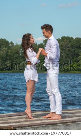 Man and woman dressed in white holding hands on a wooden pier near the water. Girl standing on tiptoe.