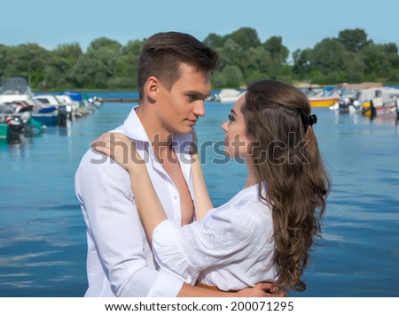 Woman hugging man and looking into her eyes against the backdrop of boats