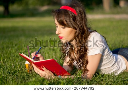 Young girl with a notepad and pen in a summer park on the grass