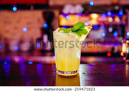 beautiful frozen cocktail glass with ice, mint and pineapple on a dark wooden bar counter, bokeh bright background