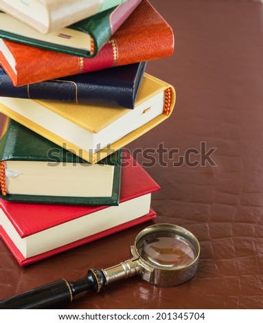 Stack of books, magnifying glass, glasses and watch on a leather background.