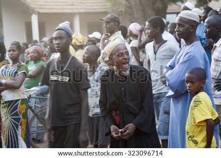 GABU, GUINEA-BISSAU - MARCH 31, 2014: Portrait of an african elder in traditional clothes and muslim caps laughing at the promises of a candidate at a political rally during 2014 general elections
