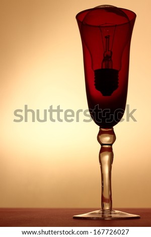 Light bulb served in red wineglass on red tablecloth in contrast light. Conceptual image representing for example idea properly served to investor etc.