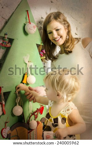Happy family of mother and baby sitting together on sofa and looking on wooden new year tree and making up tree.