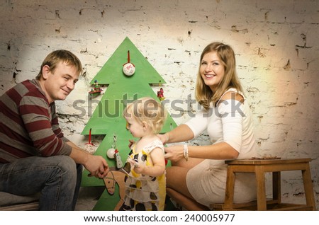 Happy family of mother father and baby sitting together on sofa and looking on wooden new year tree and decorating a Christmas tree.