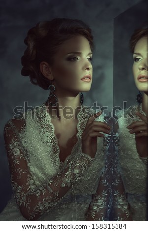 Girl in a wedding dress near the mirror. Bride looks in the mirror.