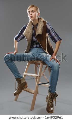 androgynous girl sits on a chair. Jeans and jacket.