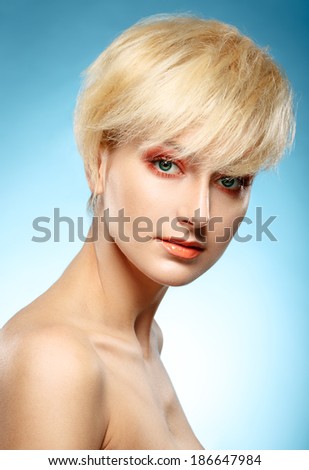 Headshot of a beautiful blonde girl with orange fashion makeup on a blue background.