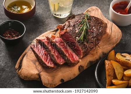 Sliced grilled meat steak New York Striploin with sauce and potato on wooden board on grey background. Barbecue steak. Medium rare meat