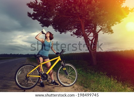 Beautiful sports girl with bike drinking water from a bottle. Style as instagram.