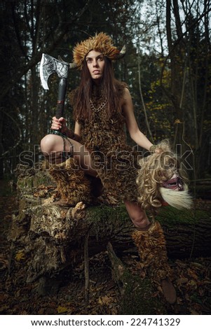 The ancient woman in the forest with an ax in his hand. Halloween. Historical costume.