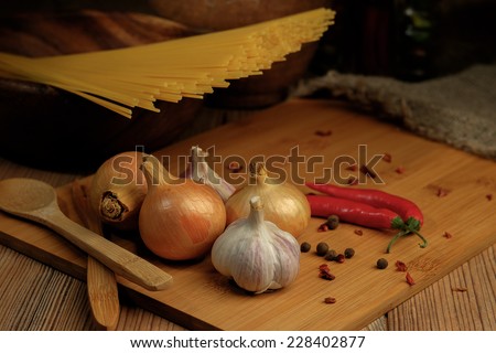 Spices assortment and spaghetti on a wooden table. Onions, garlic and chili. Shallow depth of field.