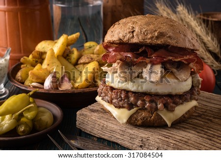 Tasty burger with beef, bacon, fried egg and mushrooms and potatoes on wooden table. Rustic style.